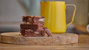 Une pile de brownies sur une planche en bois, avec une tasse jaune en arrière-plan.
