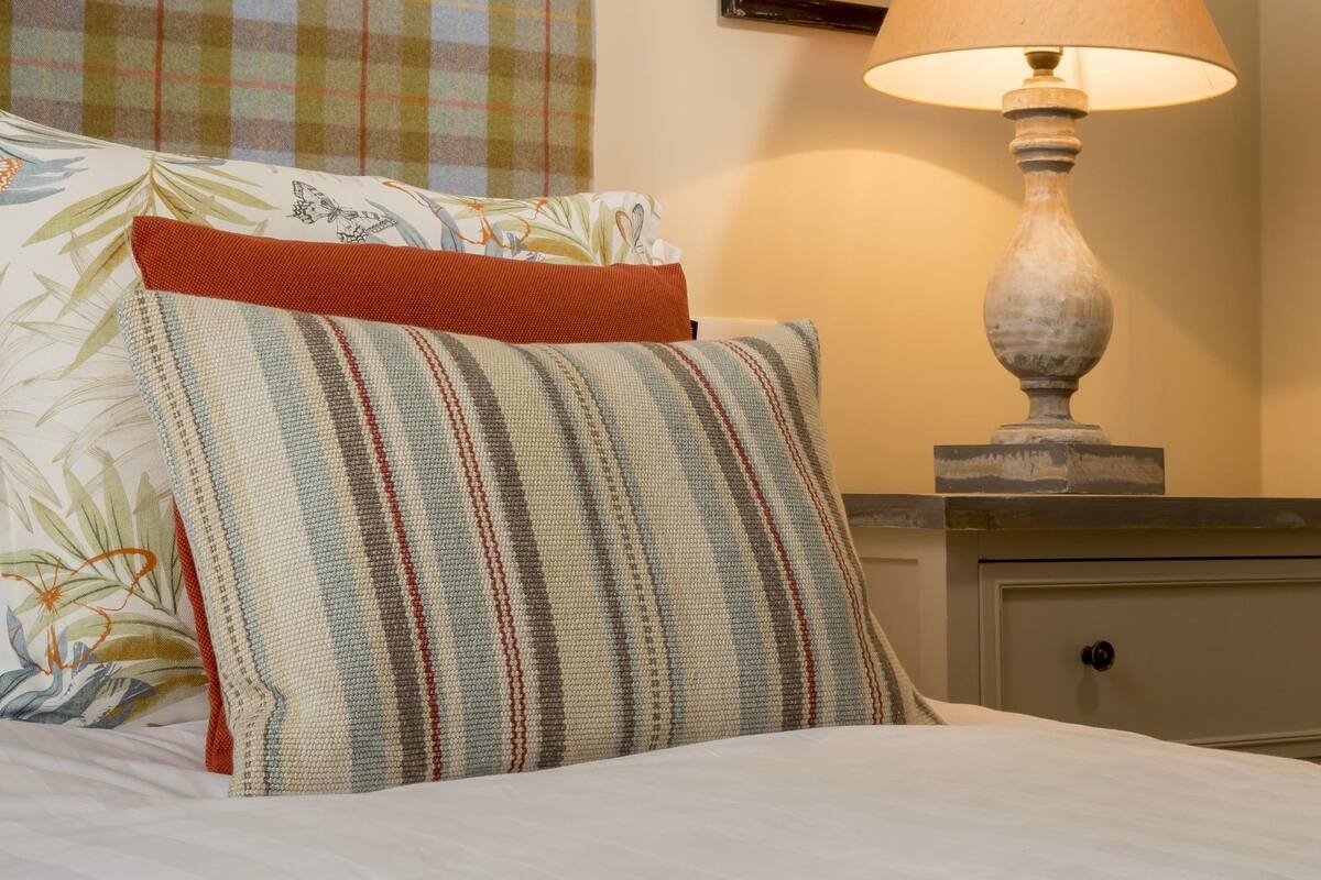 A neatly made bed with striped pillows, a plaid headboard, and a framed botanical print on the wall.