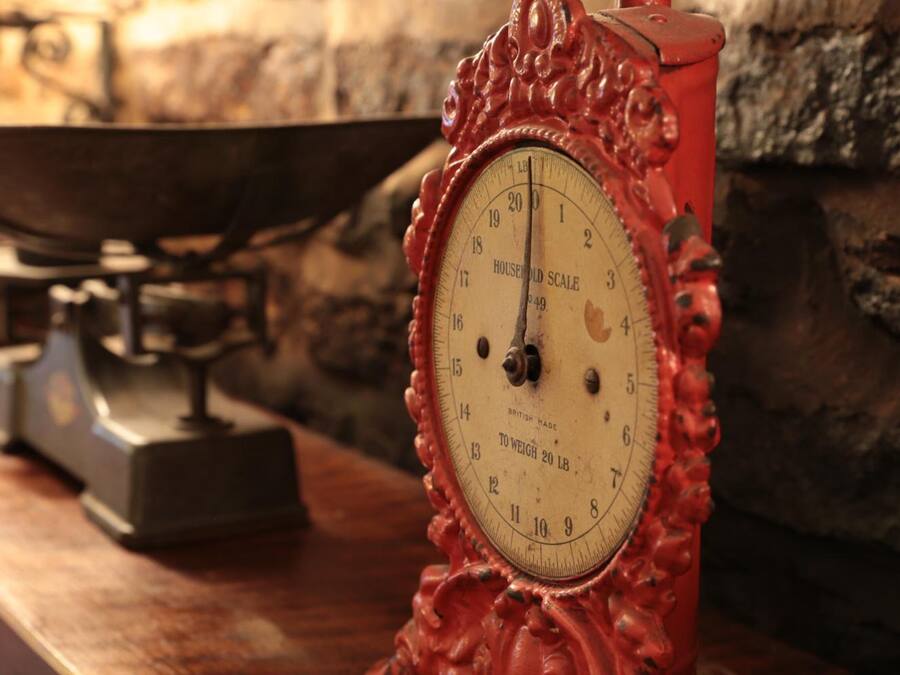 A vintage red scale with a white face, set against a stone wall background.