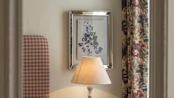 A bedroom with a bed, a nightstand with a lamp, a framed picture, and a floral curtain.