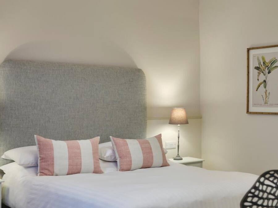 A neatly made bed with striped pillows, two bedside lamps, and framed botanical prints on the wall.
