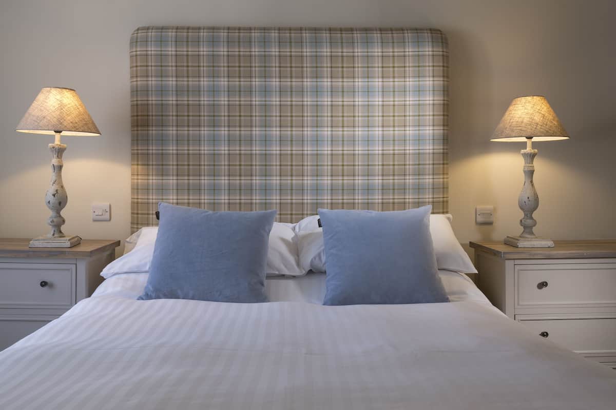A neatly made bed with a plaid headboard, two bedside tables with lamps, and a simple wall switch.