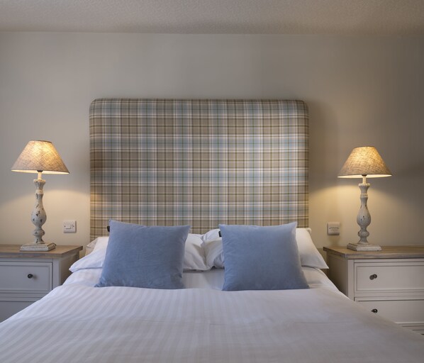 A neatly made bed with a plaid headboard, two bedside tables with lamps, and a simple wall switch.