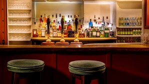 A bar area with shelves of liquor bottles, glasses, and stools. - The George (South Molton)