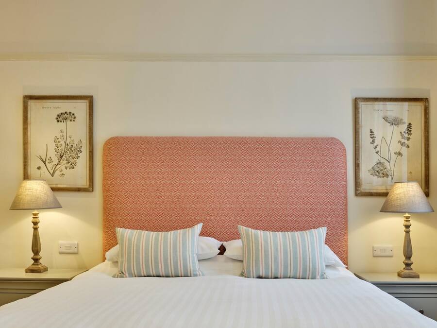 A neatly made bed with striped pillows, a red textured headboard, and two wall-mounted lamps.