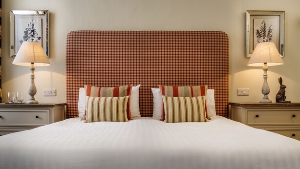 A double bed with a red checkered headboard, two bedside tables with lamps, and a framed floral artwork on each wall. - The George (South Molton)