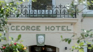 The exterior of the George Hotel with a sign above the entrance and a decorative metal railing above. - The George (South Molton)