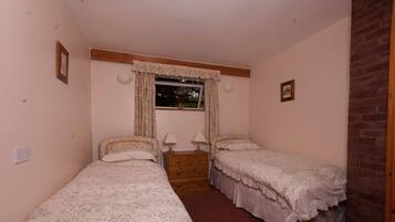 A bedroom with two single beds, a dresser, a window with curtains, and a brick wall.