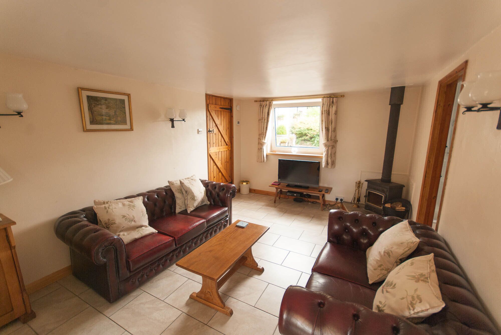 A living room with a leather sofa, a wooden coffee table, a television, and a wood-burning stove.