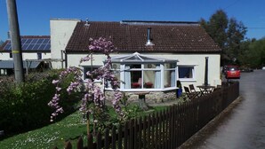 A house with a conservatory, a fenced garden, and a red car parked on the street. - Greyfield Farm Cottages (Bristol)