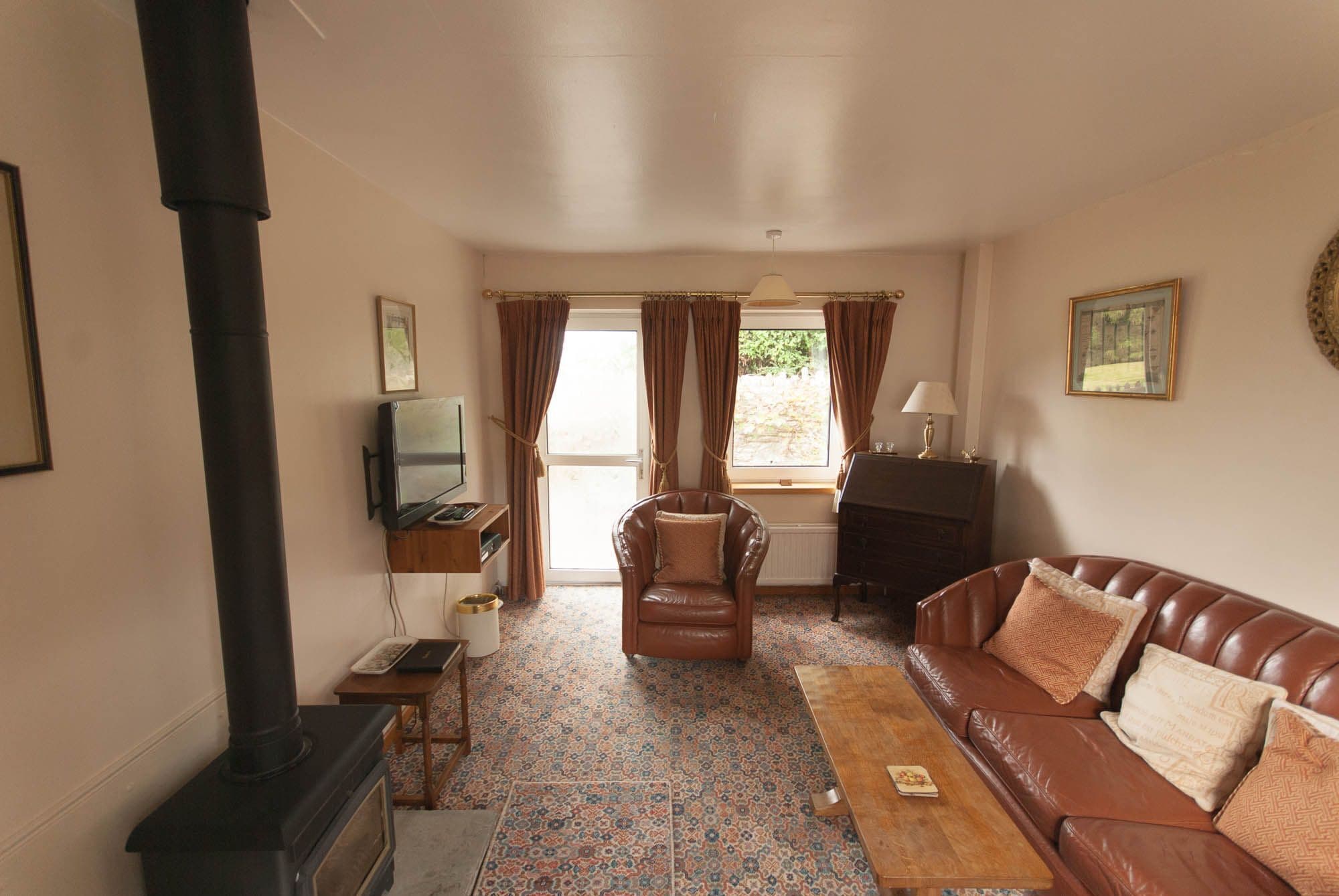 A living room with a fireplace, a sofa, a chair, a television, and a window with curtains.