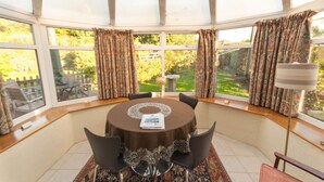 A dining area with a round table, chairs, and a view of a garden through large windows. - Greyfield Farm Cottages (Bristol)
