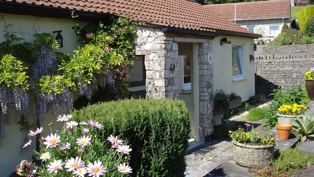 A stone house with a tiled roof, a stone entrance, and a garden with flowers and plants. - Greyfield Farm Cottages (Bristol)