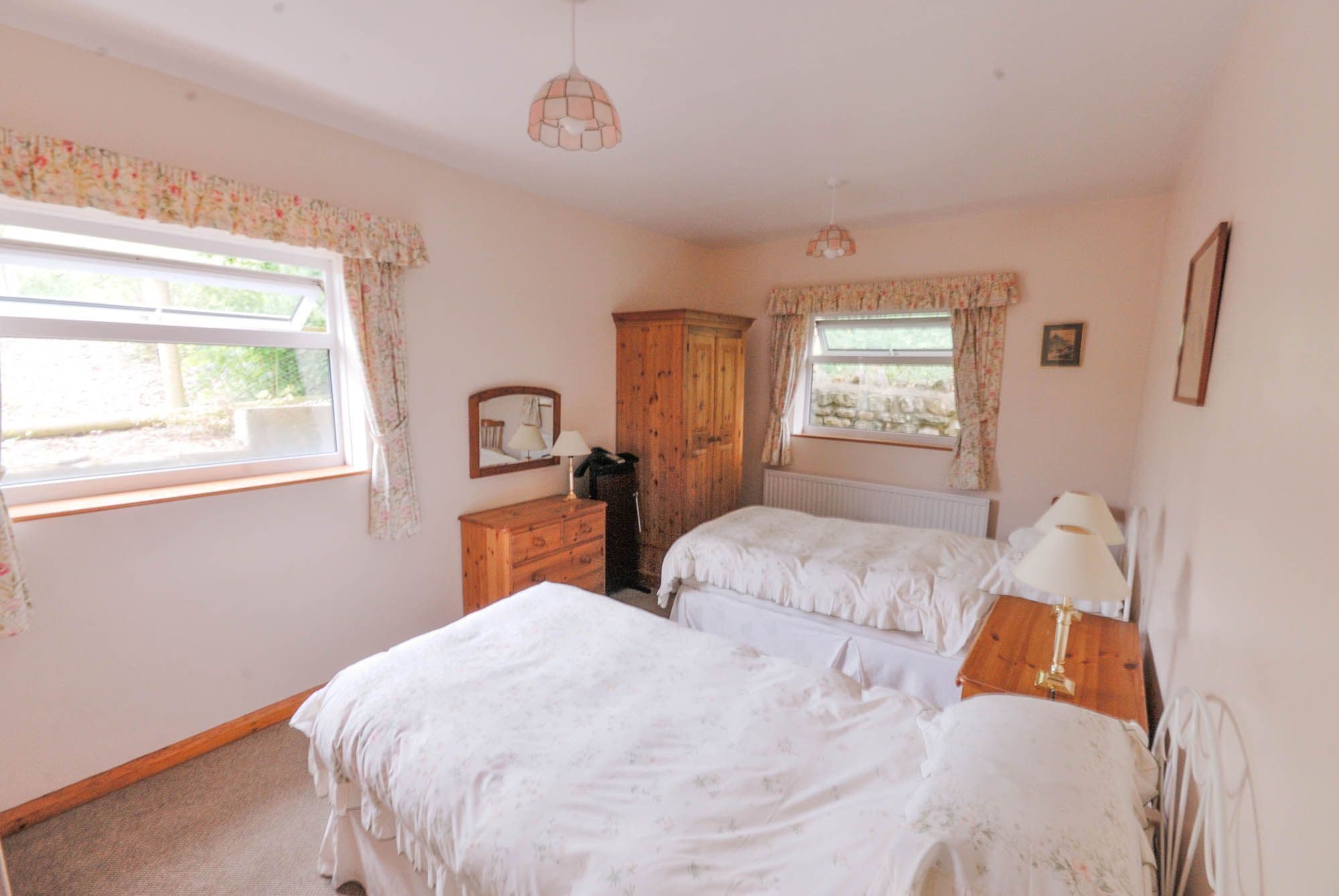 A bedroom with two beds, a wooden wardrobe, a radiator, and a window with curtains.