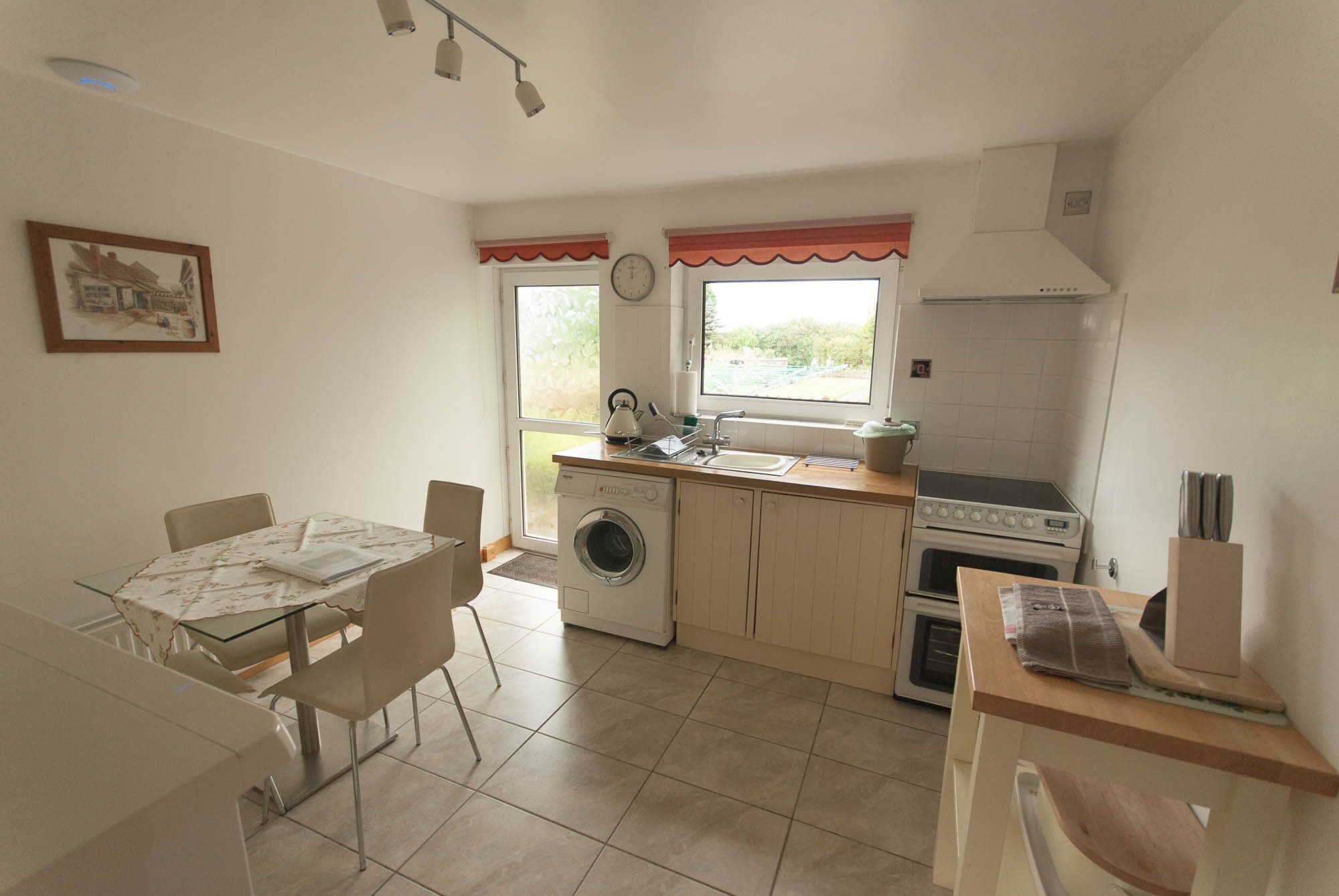 A compact kitchen with a washing machine, a stove, and a sink. There is a dining table with chairs and a window with a view.