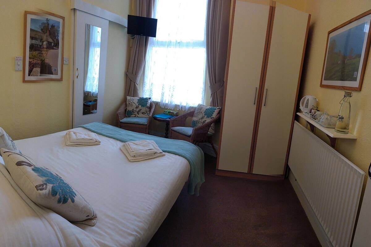 A hotel room with a bed, two chairs, a small table, a TV, and a wardrobe.