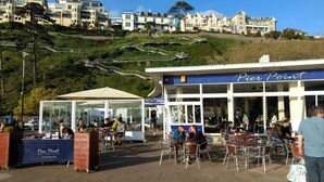 Pier Point restaurant with outdoor seating, a glass enclosure, and a view of hillside buildings. - Haven House (Torquay)