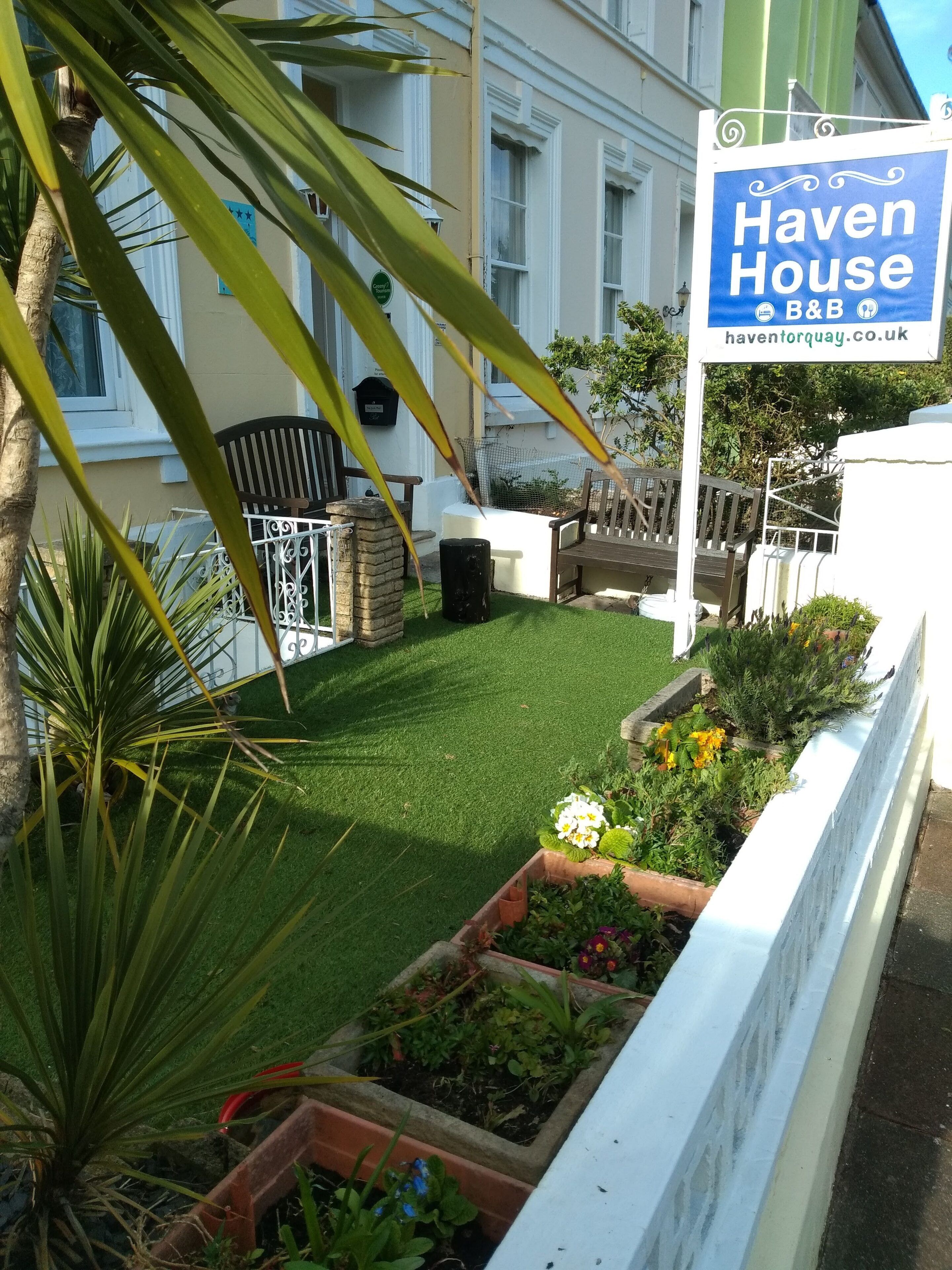 A garden with a lawn, flower beds, and a sign for Haven House B&B.