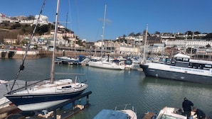 A marina with boats docked, a large offshore turbine service vessel, and a backdrop of residential buildings. - Haven House (Torquay)