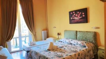 Una habitación de hotel con cama, una silla, una mesa, un cuadro y una ventana con cortinas.