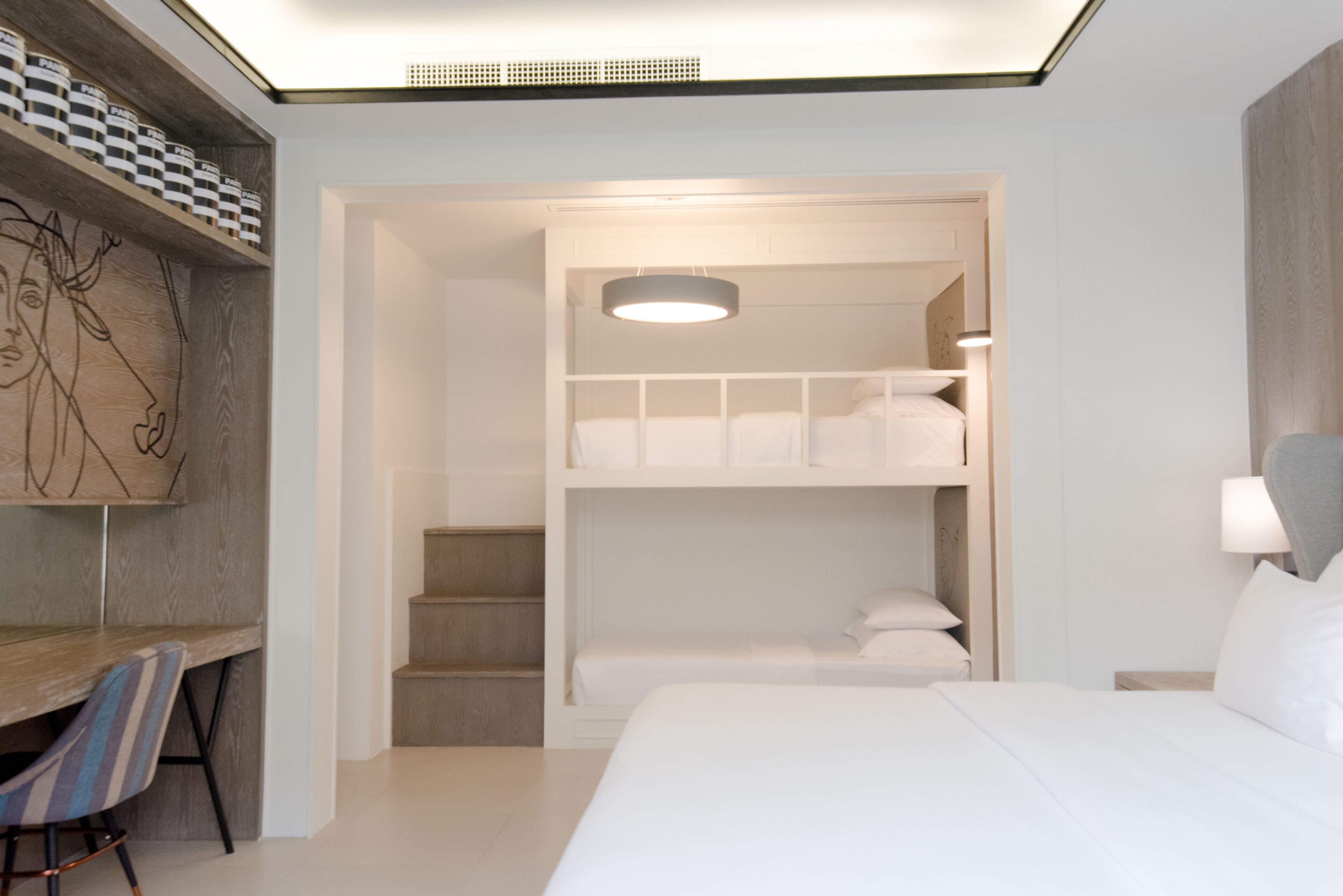 Quarto de hotel moderno com beliche, escrivaninha com cadeira e prateleira fixada na parede com recipientes.