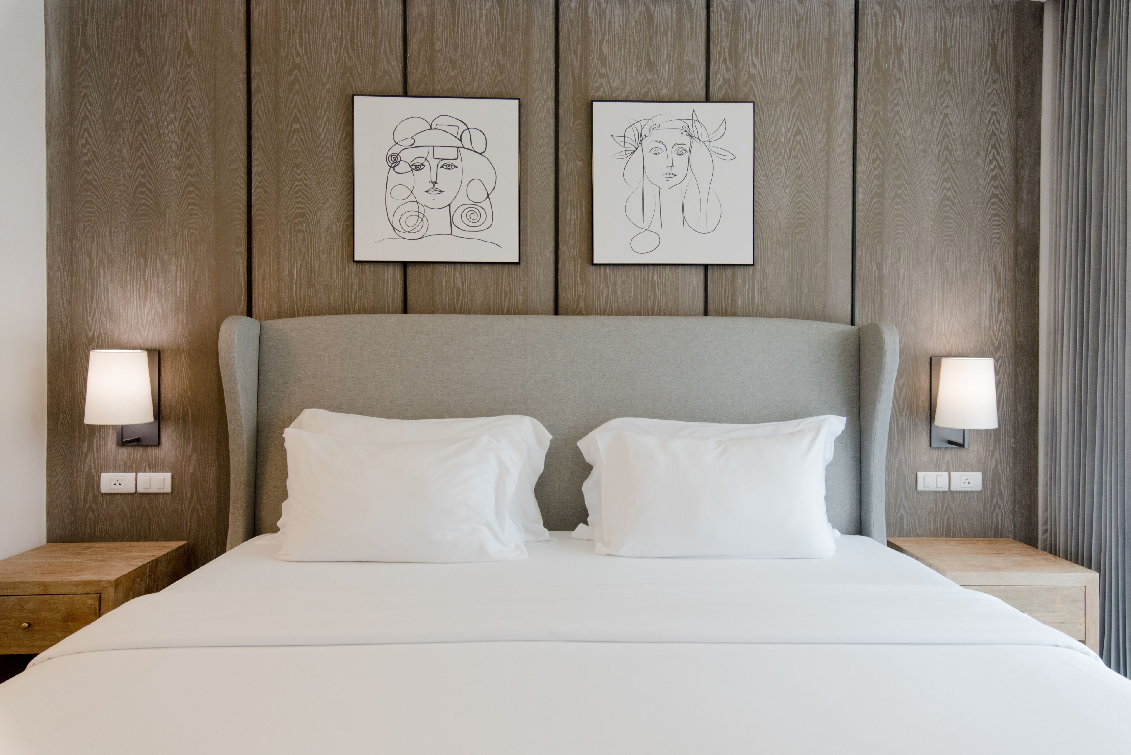 A neatly made bed with two pillows, a wooden headboard, and two bedside lamps.