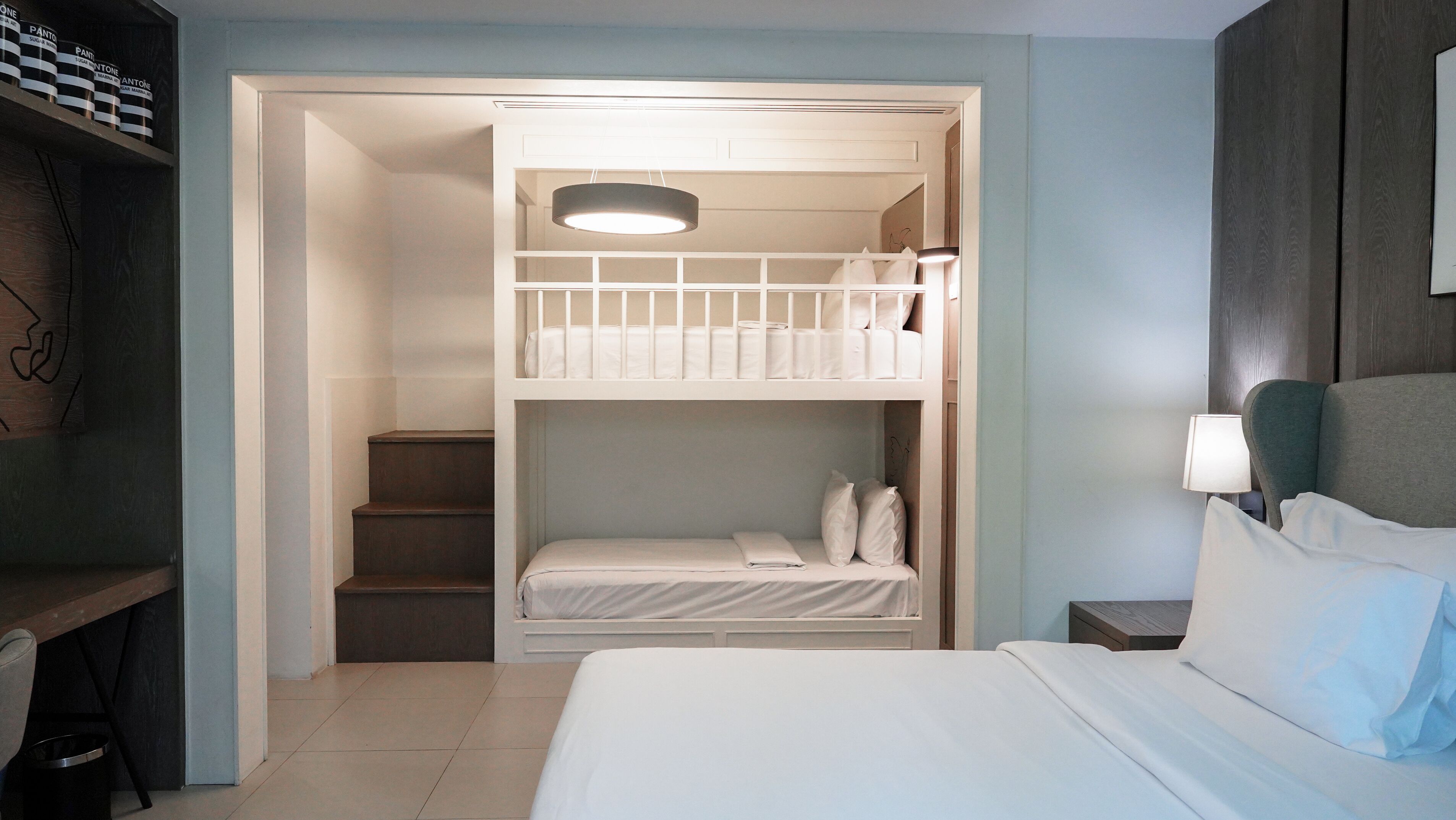 Una habitación con una cama individual, un escritorio con una silla, una lámpara y una mesita de noche.