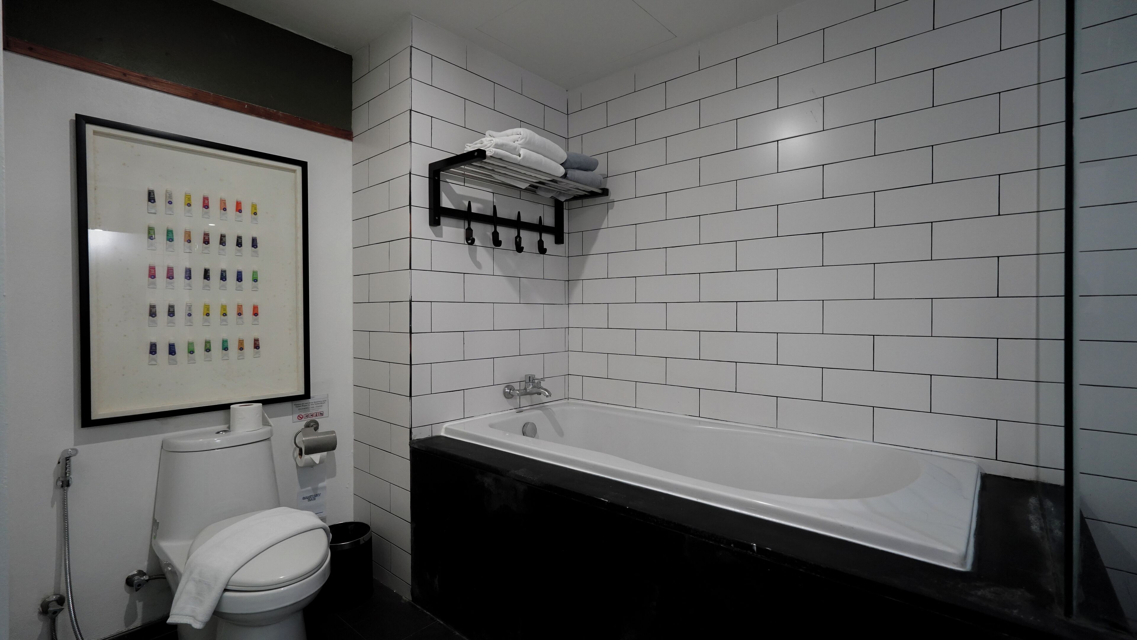 A modern bathroom with white tiled walls, a white toilet, a black bathtub, and a towel rack with towels.