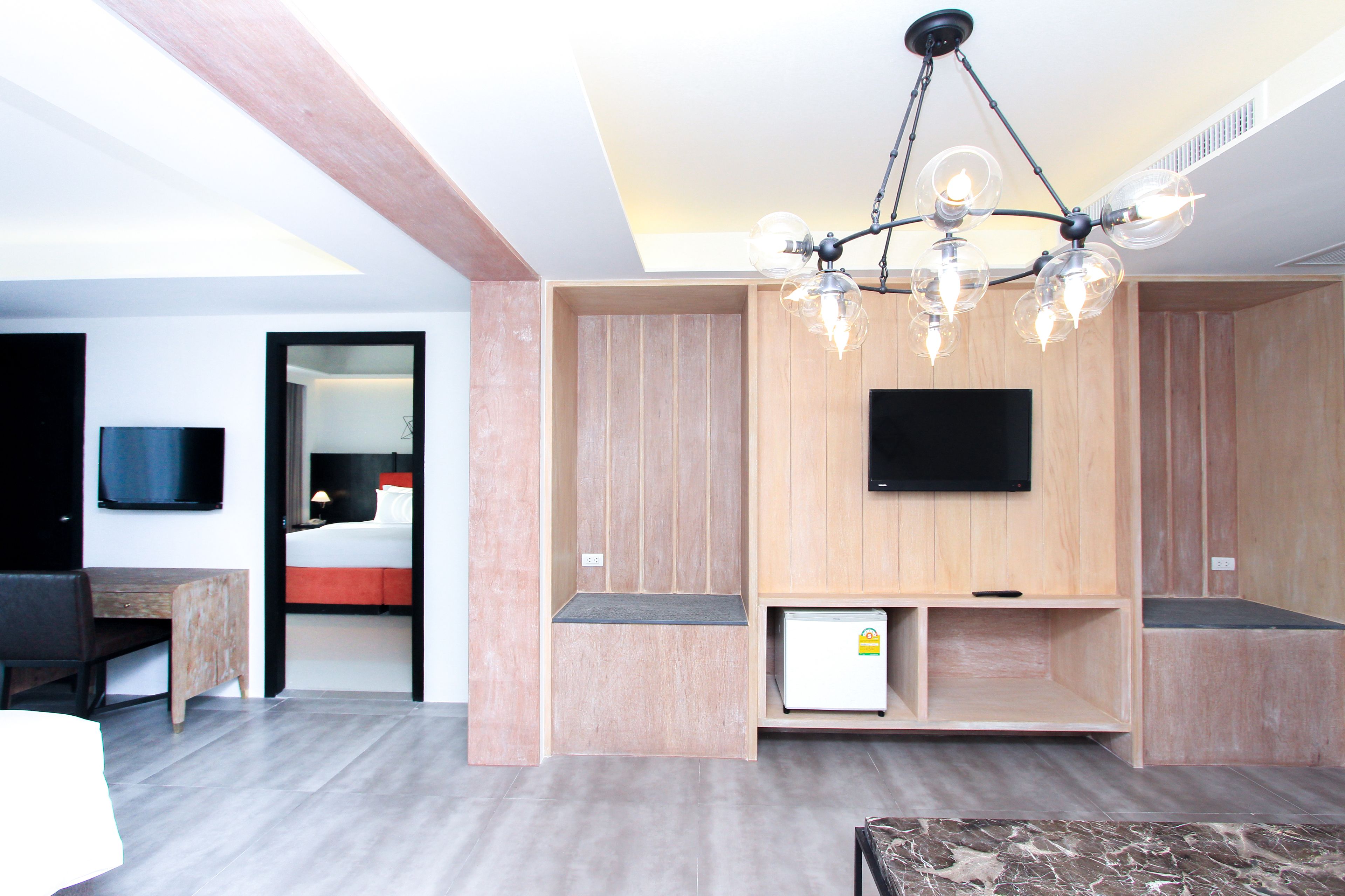 A modern hotel room with a wooden wardrobe, a flat-screen TV, a small refrigerator, and a marble-patterned table.