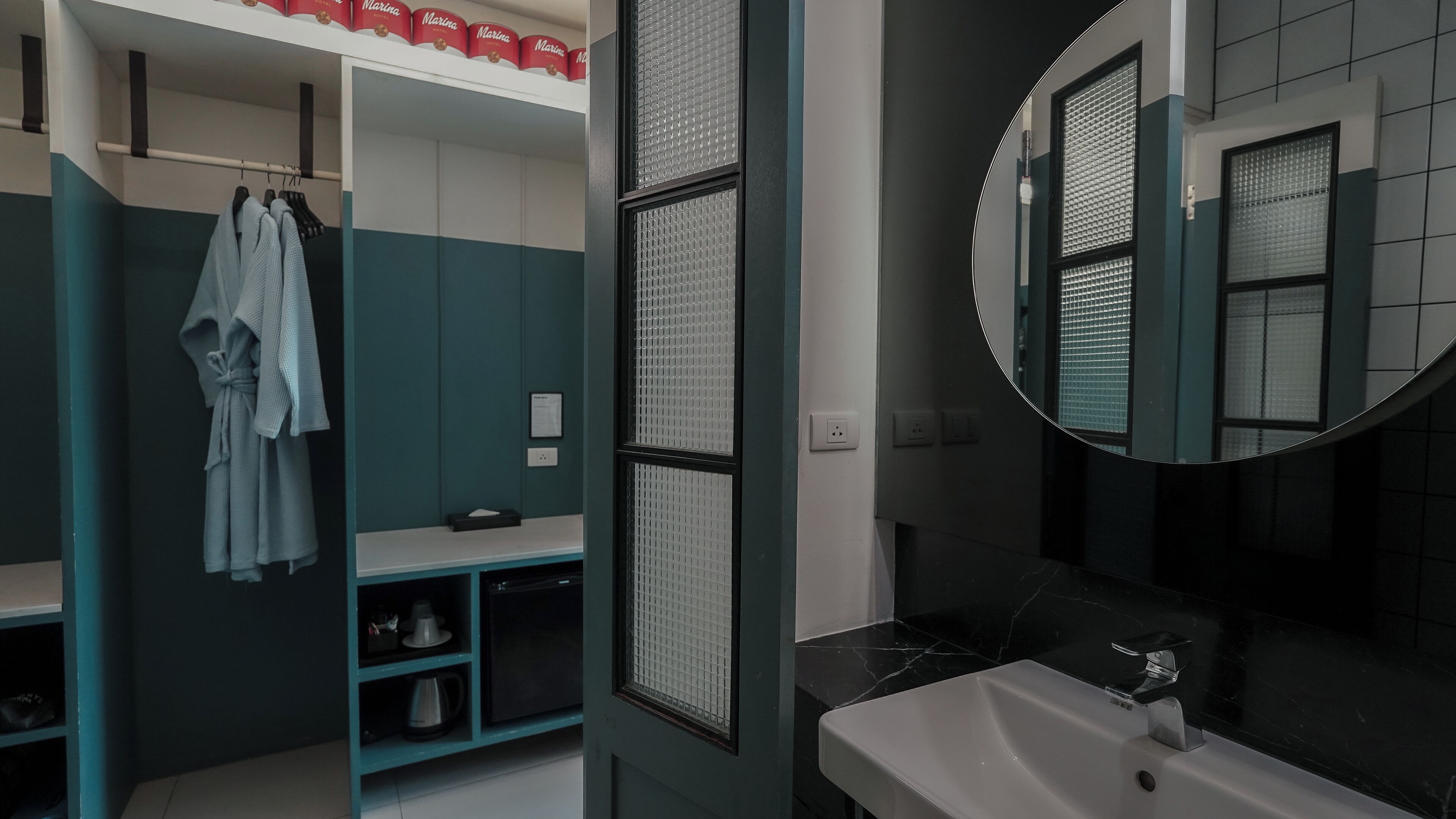 A modern bathroom with a white sink, a large mirror, and a towel rack with robes.