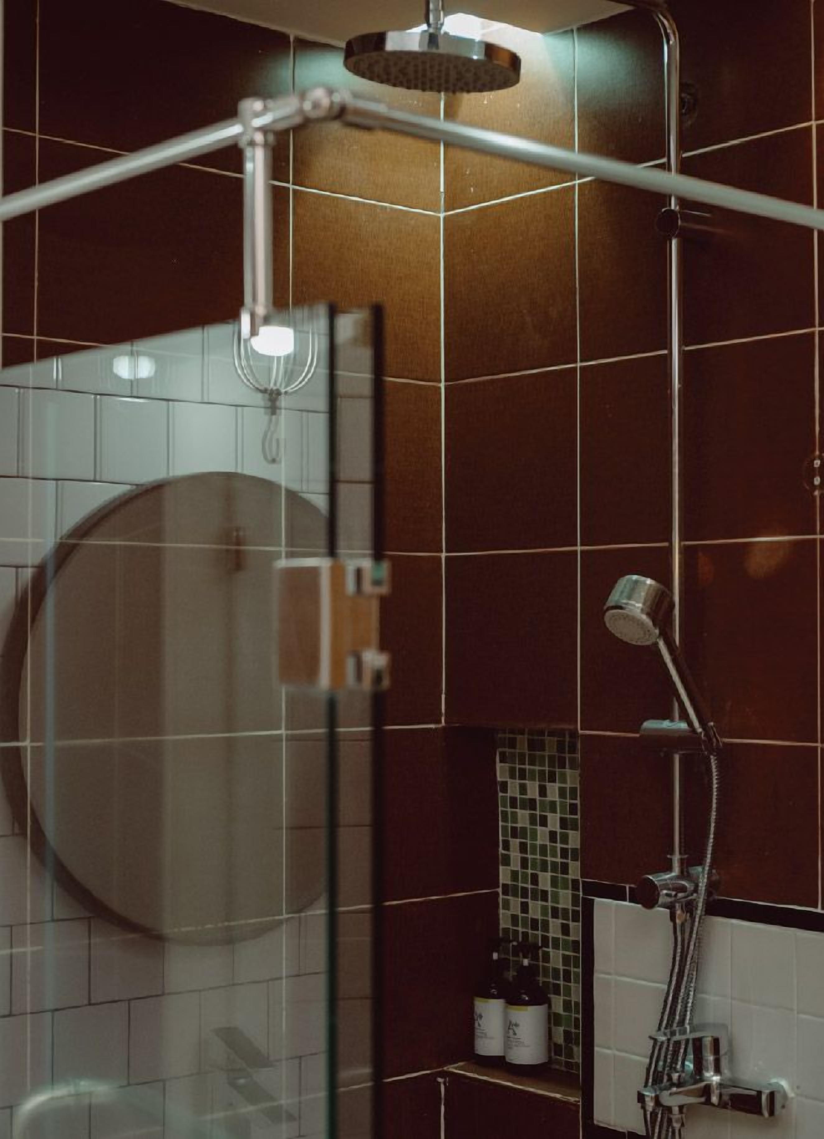 A modern bathroom with a glass shower enclosure, a handheld showerhead, and a wall-mounted faucet.