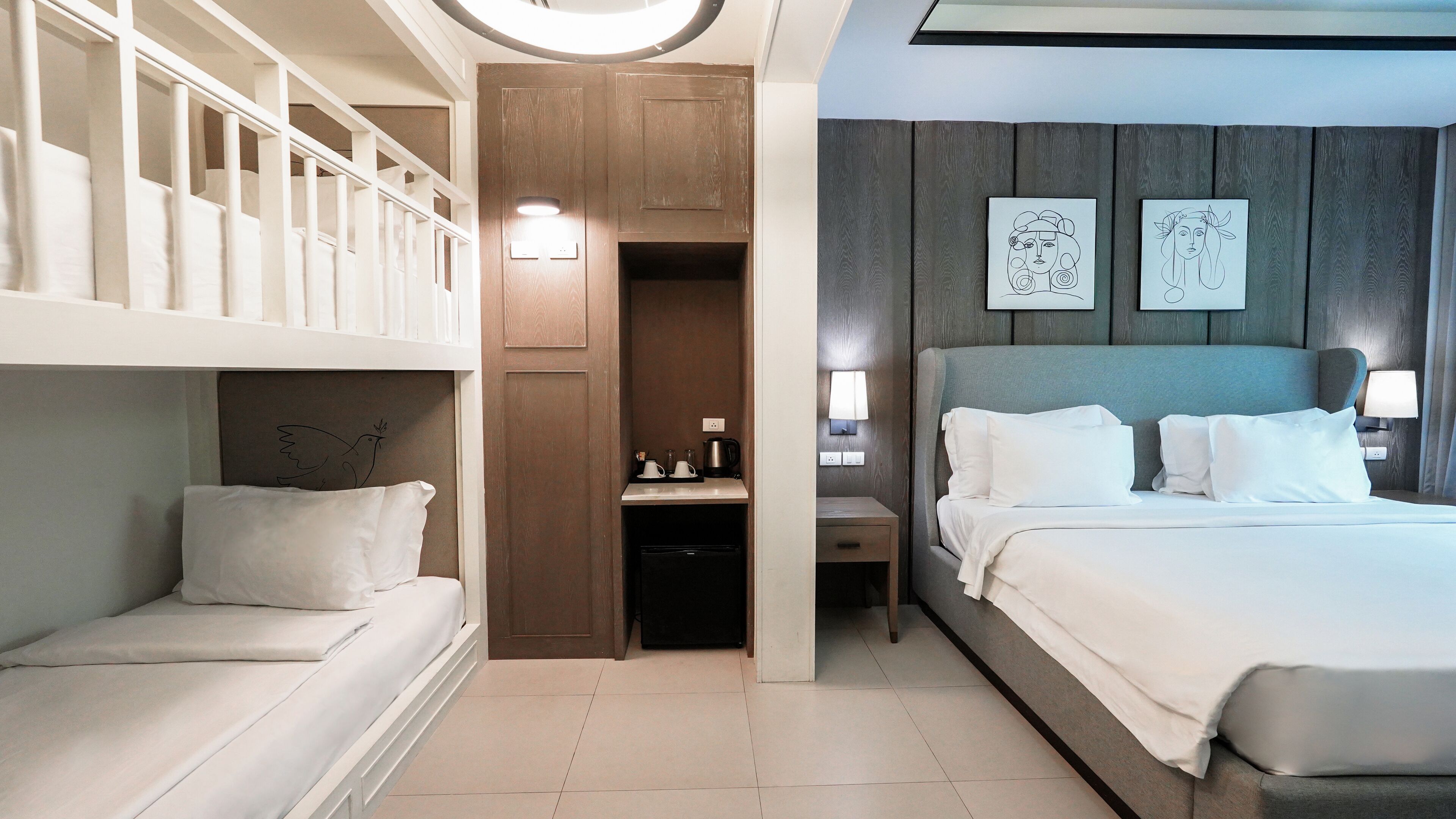 Habitación de hotel con literas, una cama individual, un pequeño rincón de cocina y dos obras de arte colgadas en la pared.