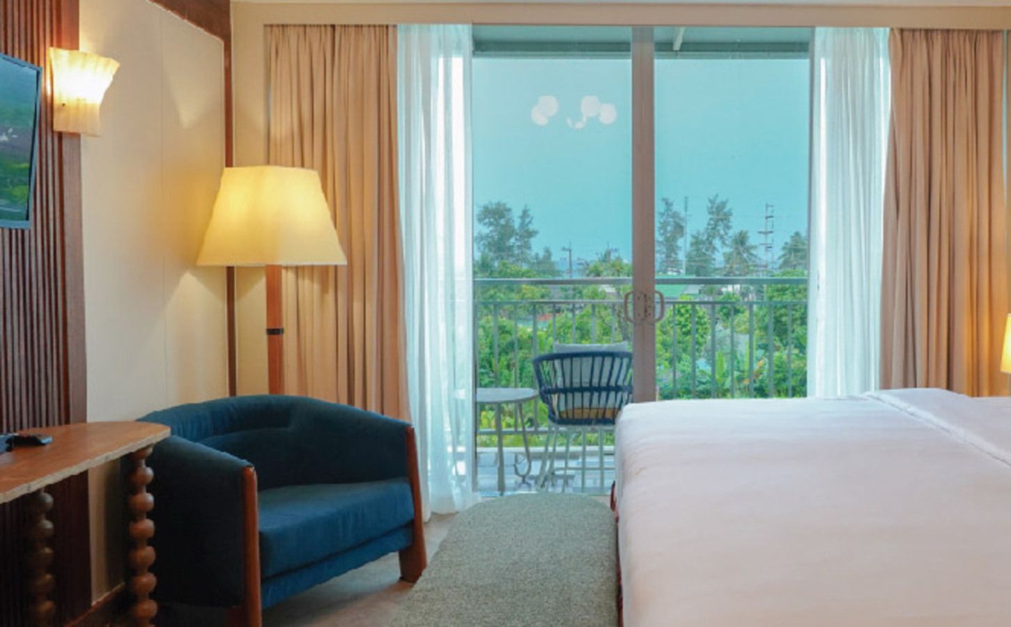 A hotel room with a bed, a desk, a chair, a balcony with a table and chairs, and curtains.