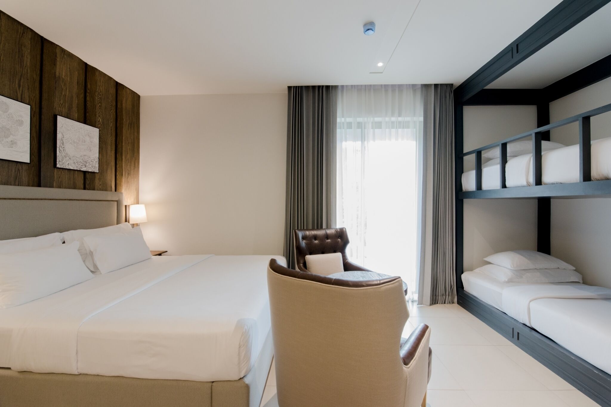 Une chambre d’hôtel avec un grand lit, une chaise, un bureau et un lit superposé.