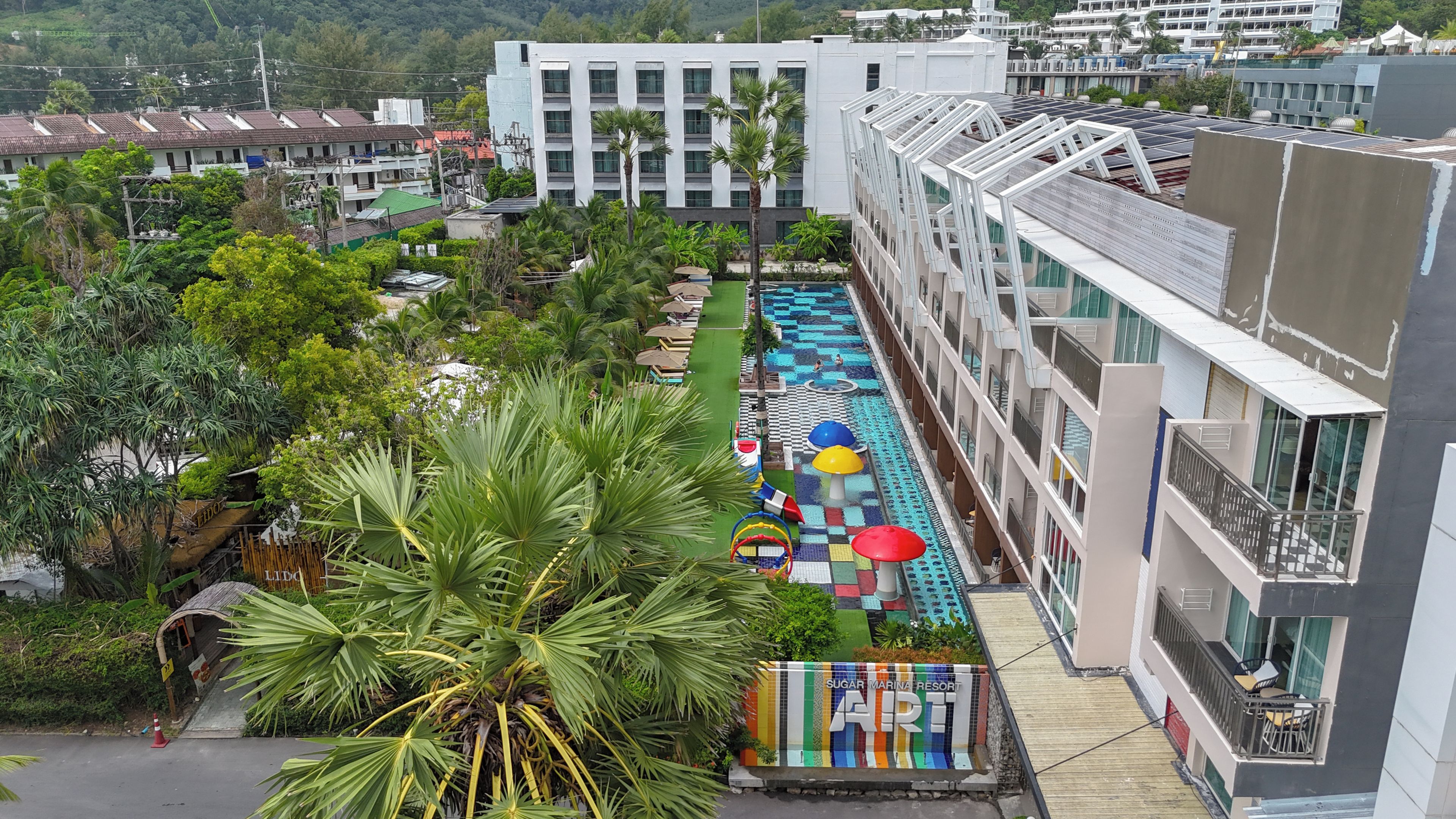 A resort with a swimming pool, palm trees, and a view of the surrounding buildings.