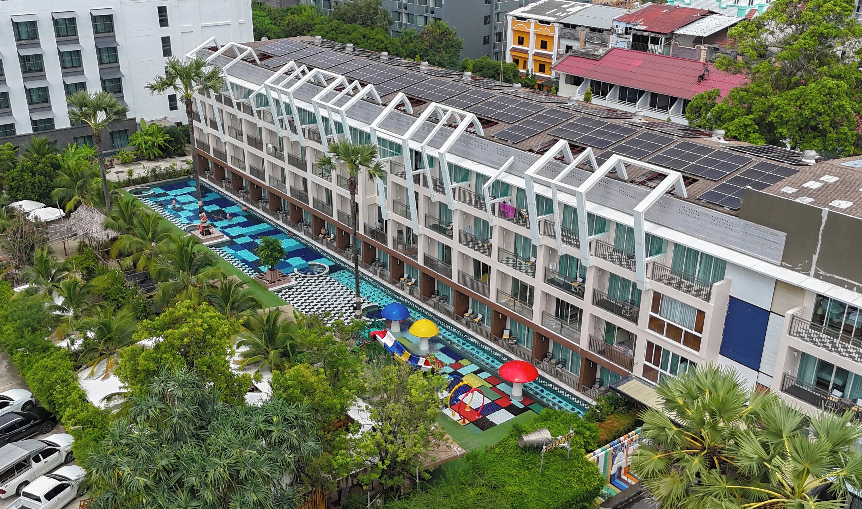 Un hôtel à plusieurs étages doté d’une piscine sur le toit, entouré d’une végétation luxuriante et de palmiers.