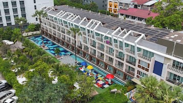 A multi-story hotel with a rooftop pool area, surrounded by lush greenery and palm trees.