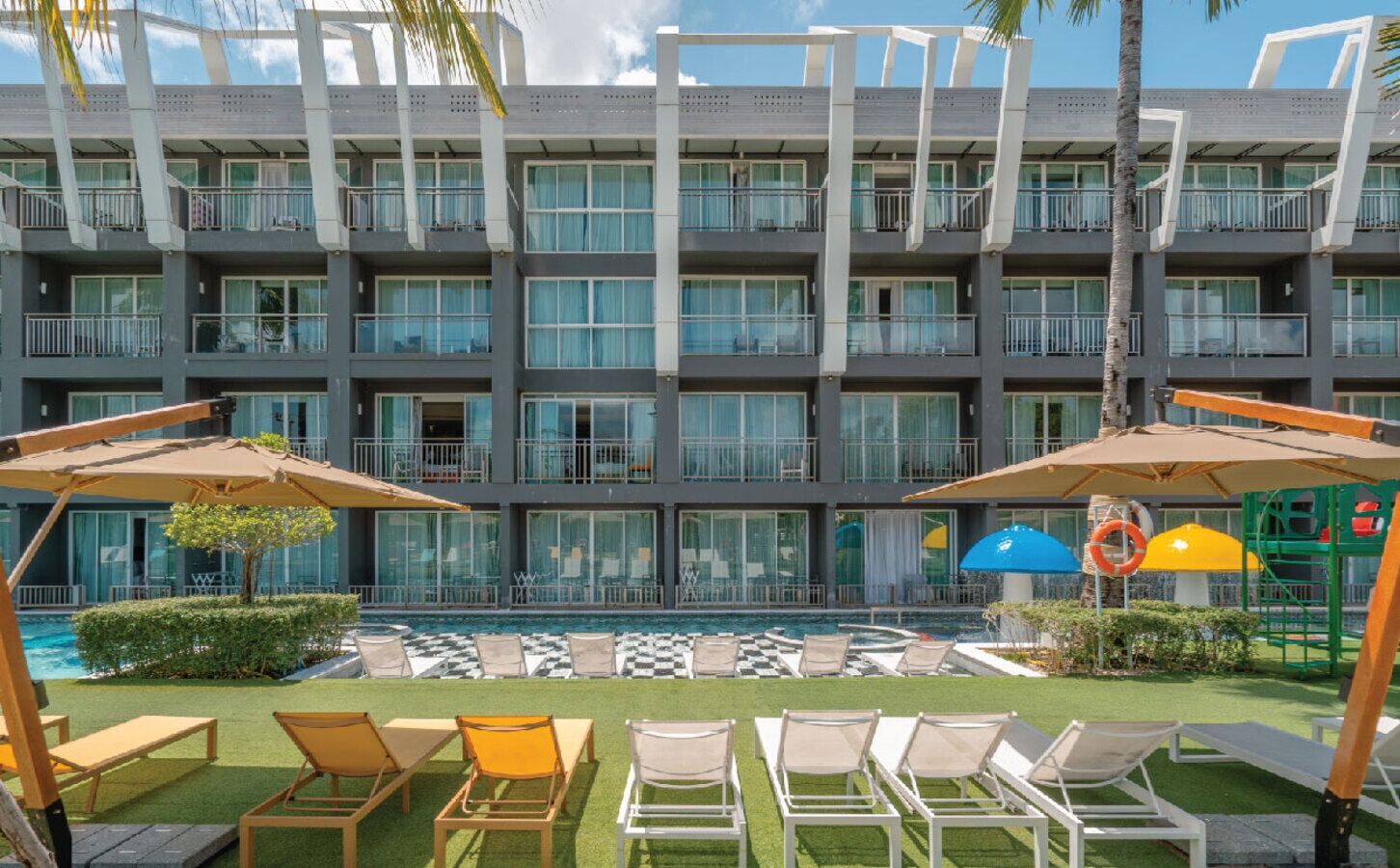 A hotel with a pool area, lounge chairs, and umbrellas.