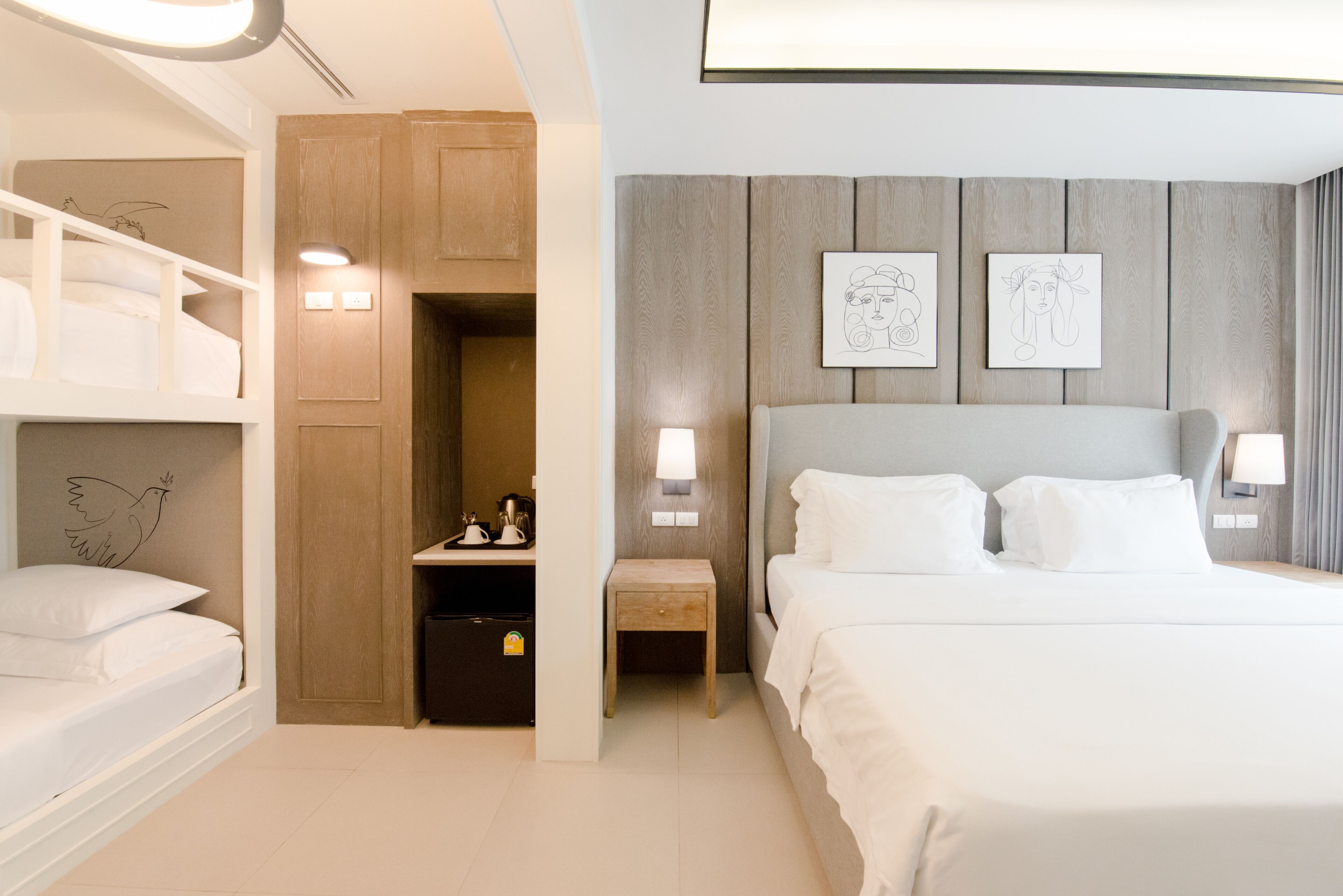 A modern hotel room with a large bed, a wooden wardrobe, a small table, and two wall-mounted lamps.