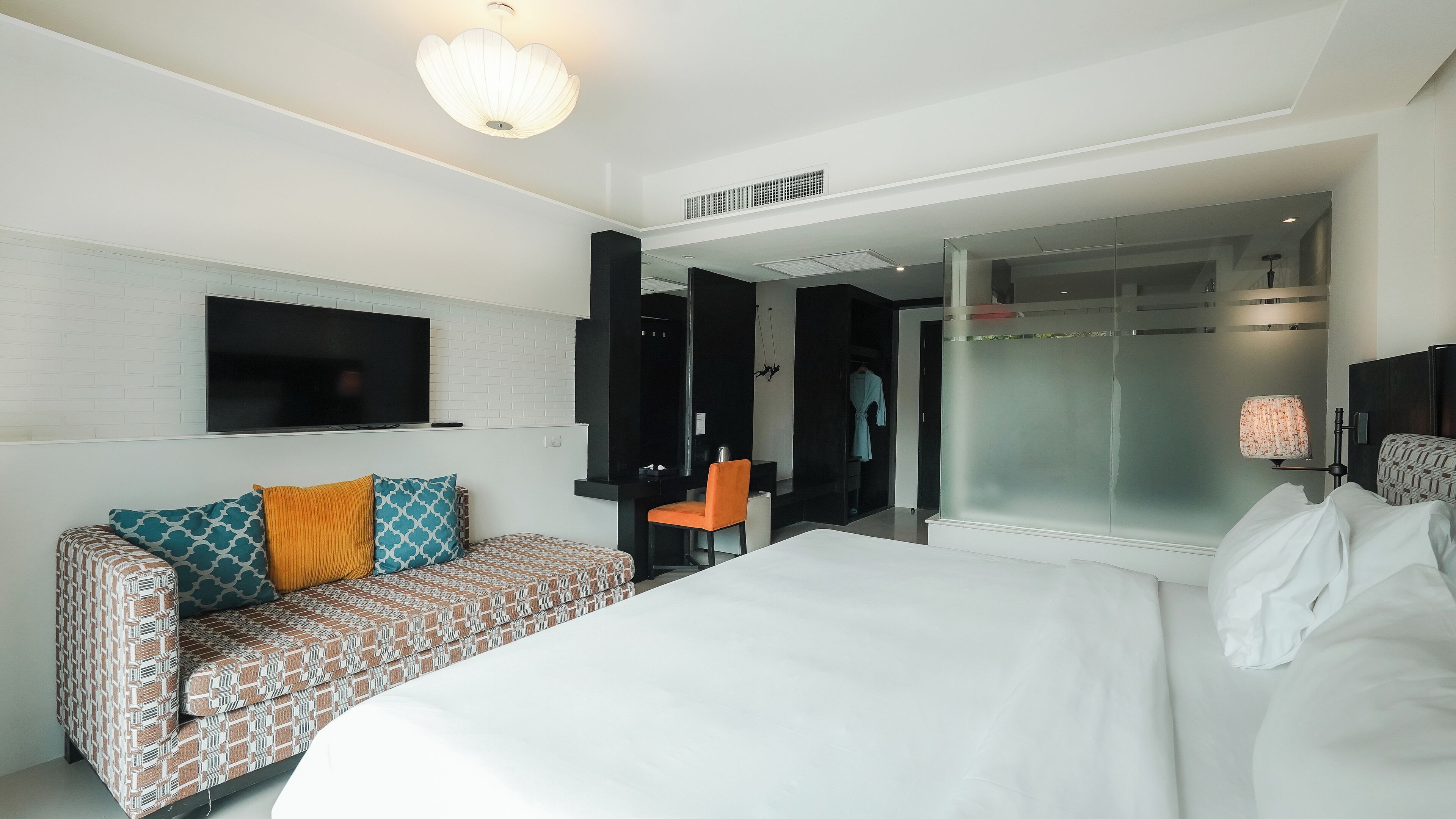 A modern hotel room with a large bed, a patterned sofa, a TV, and a shower area.