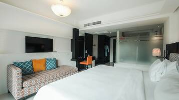 A modern hotel room with a large bed, a patterned sofa, a TV, and a shower area.
