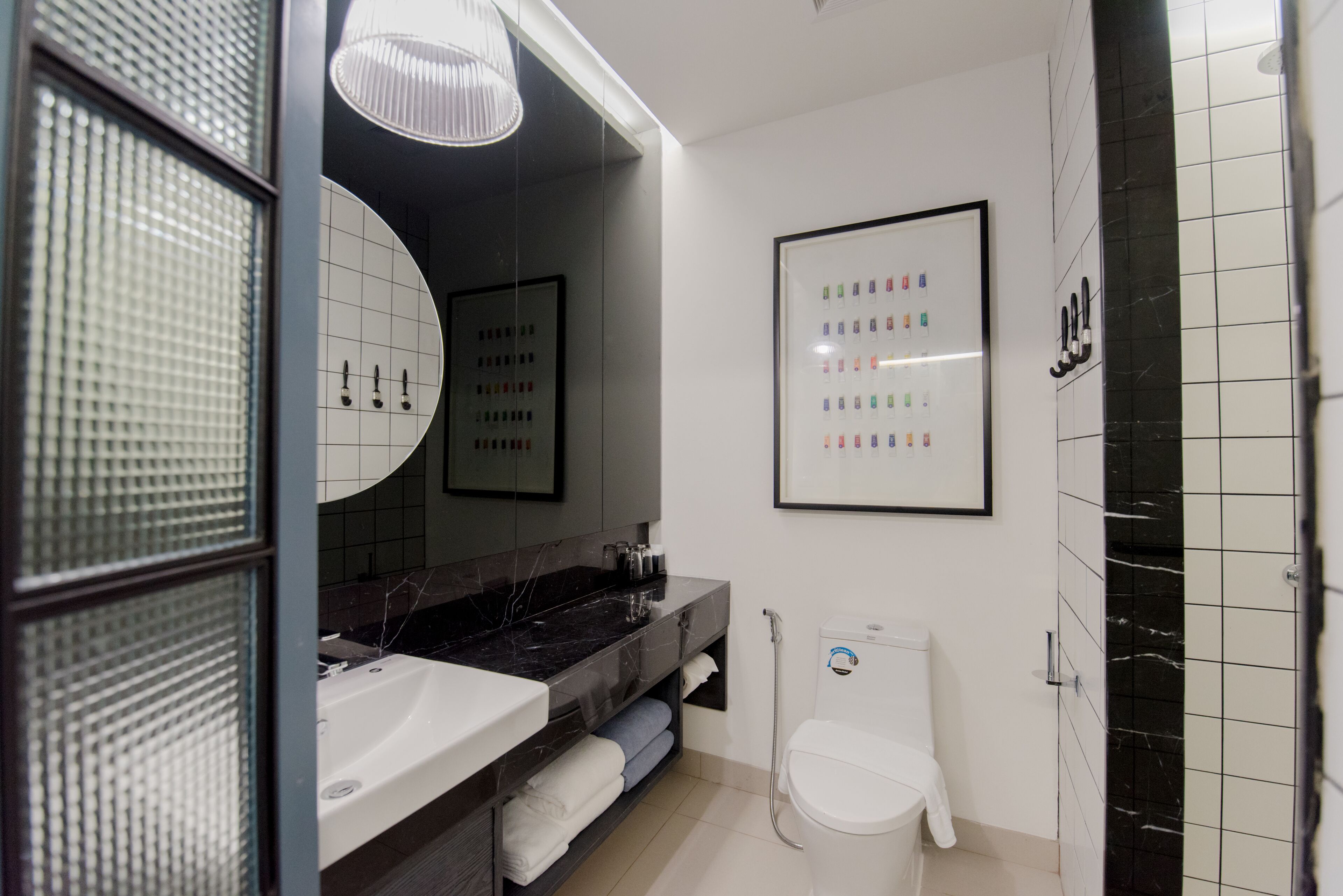 A modern bathroom with a large mirror, a white sink, a black marble countertop, a toilet, and a framed picture on the wall.