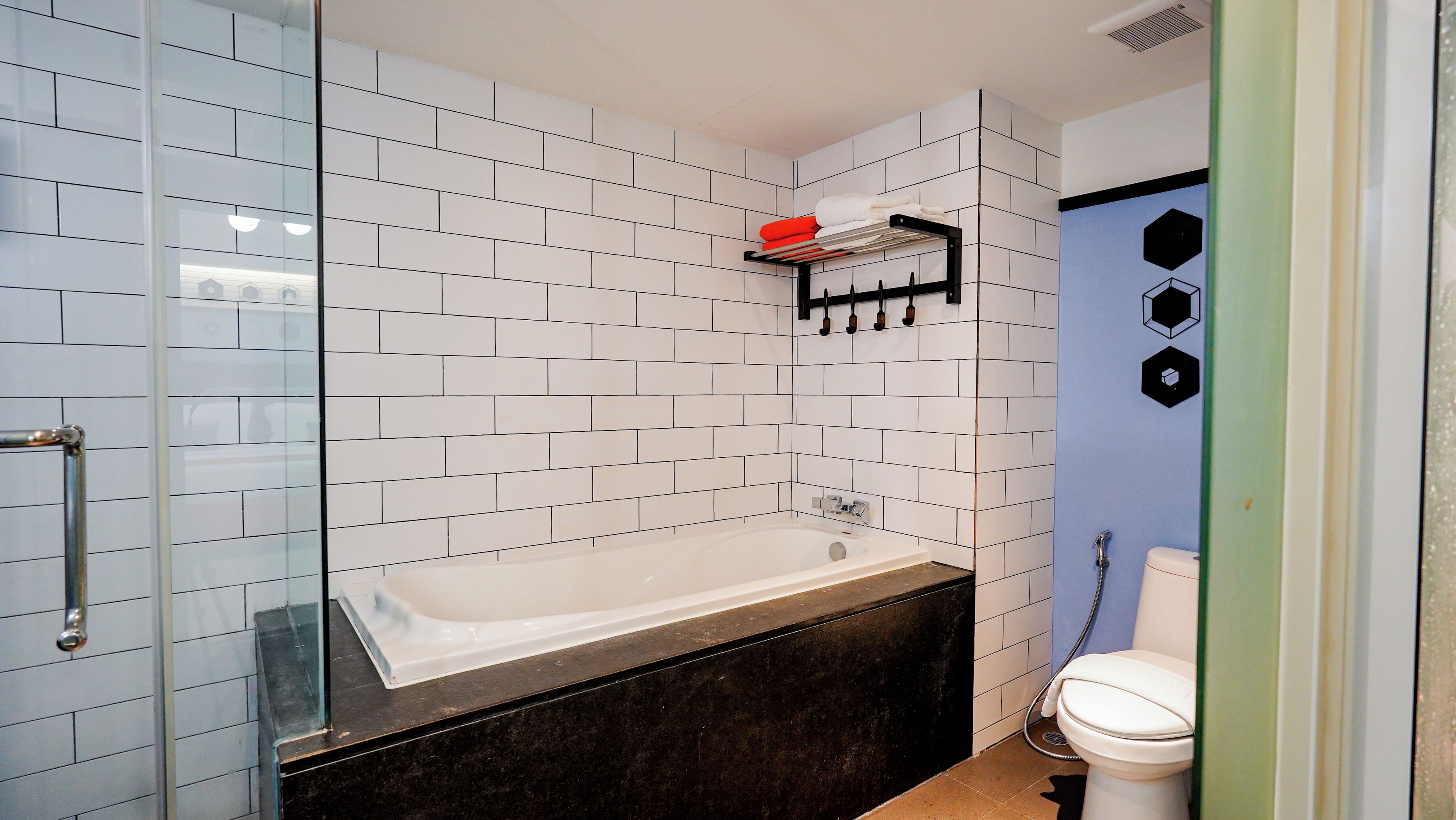 A modern bathroom with white subway tiles, a black bathtub, a glass shower enclosure, and a toilet with a blue accent wall.