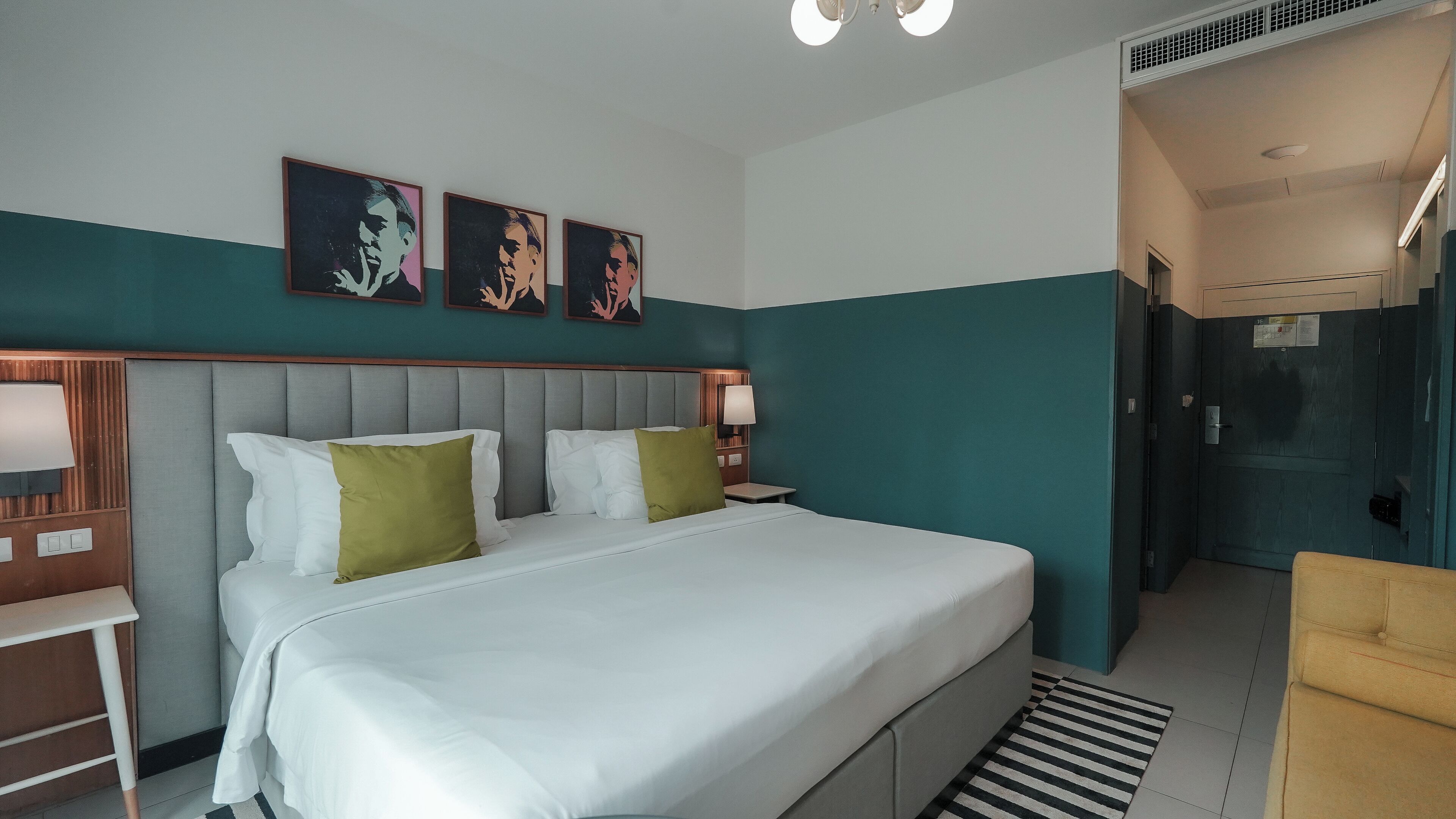 Una habitación de hotel con una cama grande, dos mesitas de noche con lámparas, un cabecero y tres obras de arte enmarcadas en la pared.
