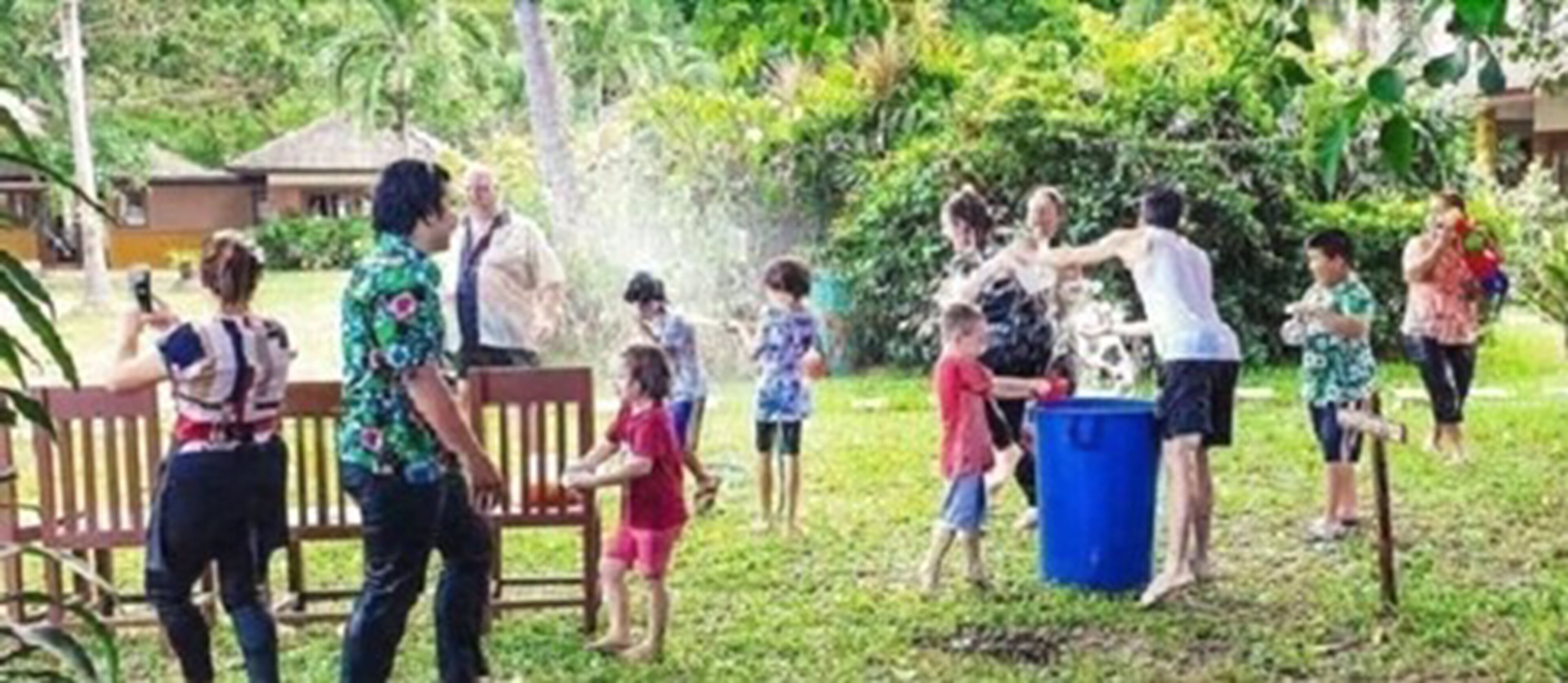 A group of people outdoors, some standing and some sitting, with a blue trash bin in the foreground.