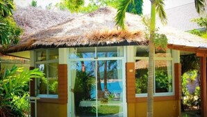 A modern building with a thatched roof, large windows, and a well-maintained garden. - Anahata Resort Samui (Koh Samui)