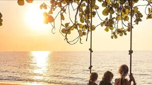 A beach scene with a swing set and three people sitting on it. - Anahata Resort Samui (Koh Samui)
