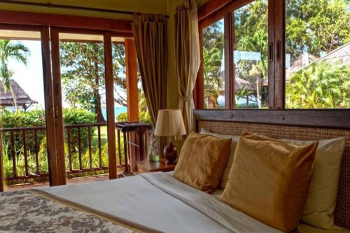 A bedroom with a bed, curtains, and a view of greenery outside.