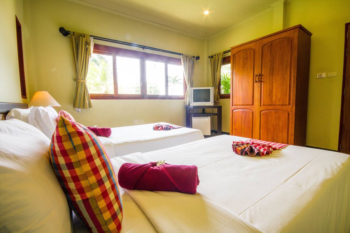 A hotel room with two beds, a television on a stand, and a wardrobe.