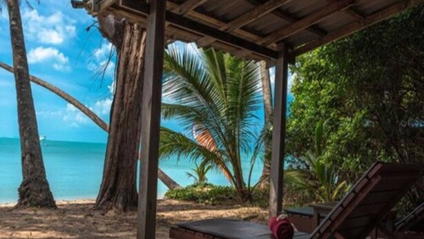 A beachside lounge with a wooden canopy, a lounge chair, and a small table. - Anahata Resort Samui (Koh Samui)